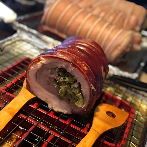A large, stuffed pork belly roll with crispy skin rests on a red and black grill rack.