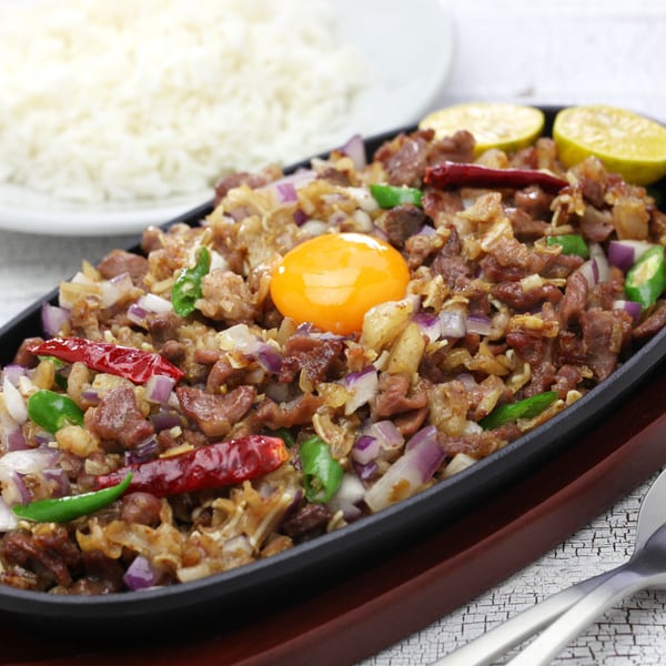 Sizzling sisig with a raw egg yolk, red onions, green chilies, and lime, served with rice.
