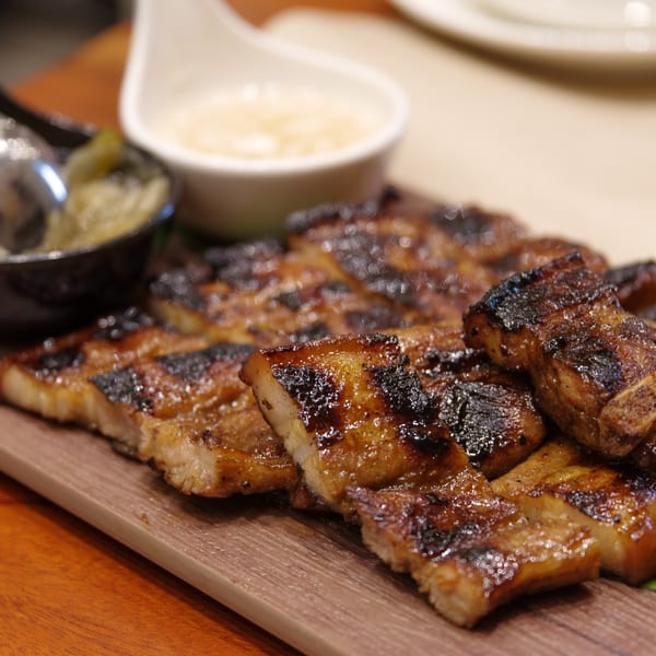Grilled pork belly slices with crispy skin, served with dipping sauces on a wooden board.