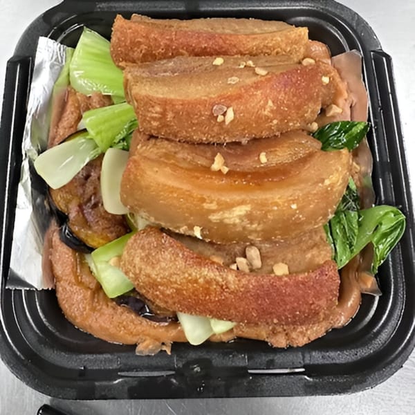 Crispy pork belly slices with bok choy and sauce in a black takeout container.