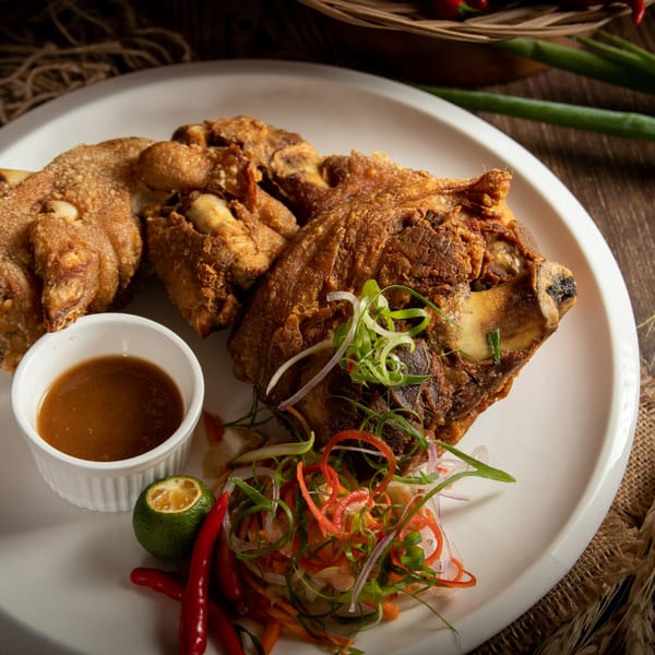 Crispy fried pork hock, garnished with sliced onions, peppers, and a side of dipping sauce.